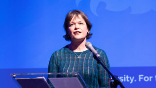 Professor Rachel Pain presenting on stage at a conference.