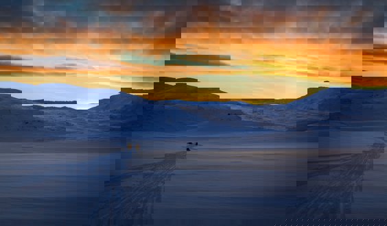 Snow capped mountain with people on snow mobiles and a sunset sky