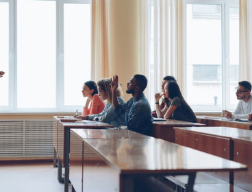 Students sitting at desks listening to someone standing in front and talking.