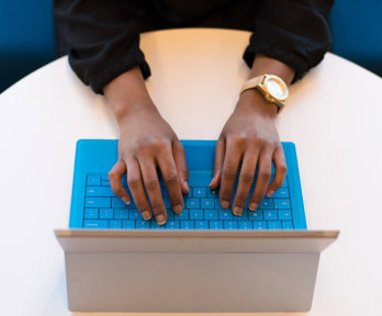 A person typing on a laptop positioned on a round, white table.