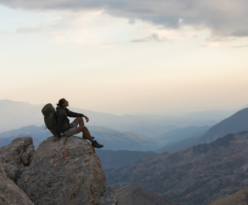 Backpacker sitting on a rock looking at the view of a mountain range.