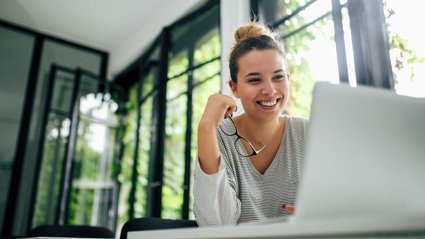 Person holding glasses smiling while looking at a laptop screen.