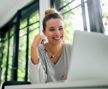 Person holding glasses smiling while looking at a laptop screen.
