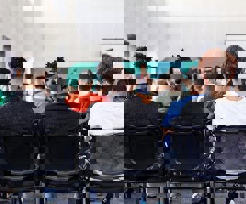 Students sitting in a classroom watching a teacher, viewed from behind