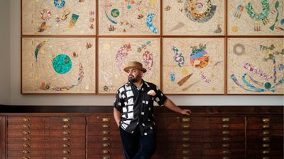 Artist Hormazd Narwiella stood in front of map drawers and modern art.