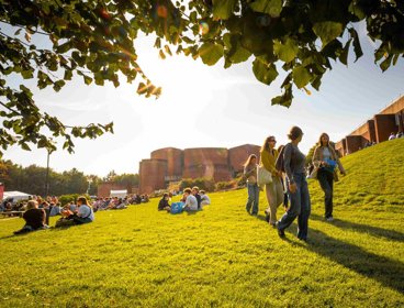 University of Sussex campus showing buildings and students sitting and walking on the grass.