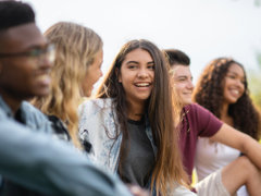Group of five young people sitting outdoorsk, with the focus is on a brown-haired person in the centre.
