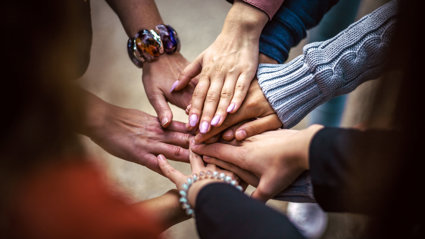 A group of people laying their hands of top of each others hands to indicate a team.