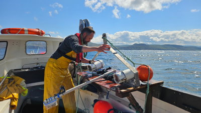 Someone in yellow overalls inspects equipment on a boat in Scotland.