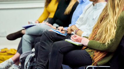 People sat with notebooks listening to a presentation and taking notes.