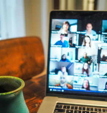 A cup next to a laptop with a blurry screen showing different people who are in an online meeting.