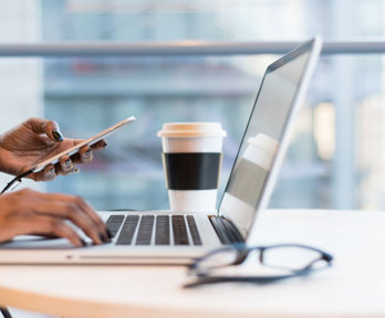 Close-up of a person holding a phone and using a laptop.
