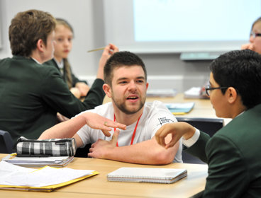 A male geography ambassador crouching down next to a male student, talking to them about geography