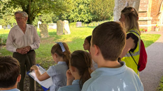 Children are listening to a man speaking and writing things down.