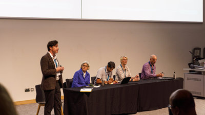 Panellists on stage at the annual conference in 2025 in Birmingham. There are four people seated and one standing