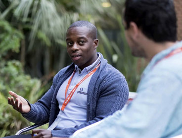 Two people having a conversation. One person on the right is sitting with their back to the camera and is blurred out.