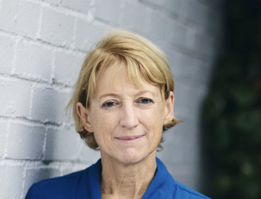 Person wearing a blue cardigan leaning against a white brick wall outdoors.