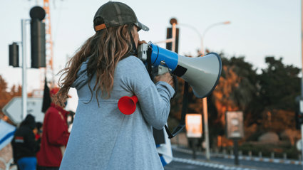 Person speaking into a microphone with a blurred background showing other protesters