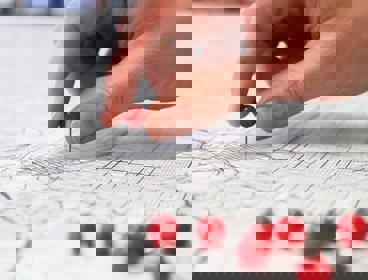 Person holding a round red pin and placing it on a map