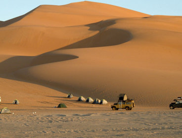 An expedition camp set up in the desert against a backdrop of high sand dunes.