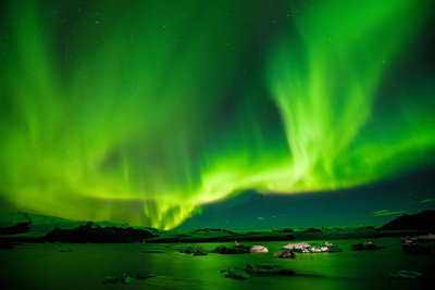 The northern lights shiining brihght green and yellow over a rocky landscape next to the sea