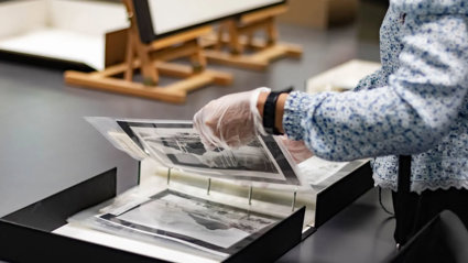 A researcher wearing archival gloves viewing historic photographs in a folder.