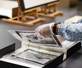 A researcher wearing archival gloves viewing historic photographs in a folder.