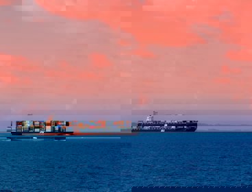 A cargo ship on the ocean with a pink sky