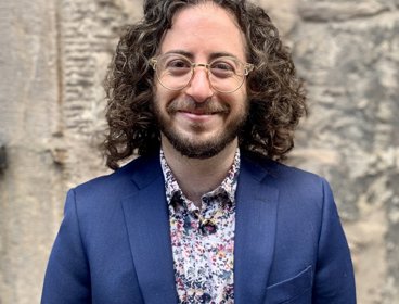 Person wearing a blue jacket and patterned shirt against a stone wall