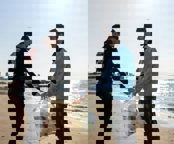 Two people on a beach holding a bag full of plastic rubbish