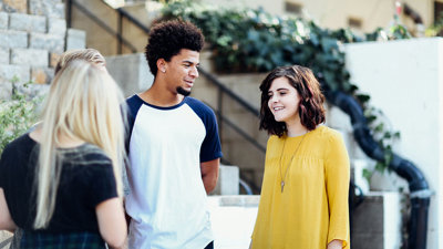 Three people talking outside in front of a set of stairs.