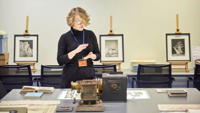 A person standing next to a table with books, glass slides, and scientific instruments on top of it.