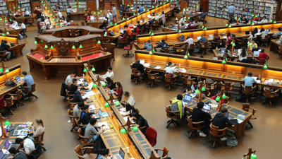 Rows of students working at long desks in a library as seen from above.