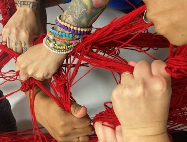 Hands holding onto intertwined strands of knitting wool.