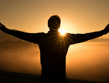 Silhouette of person standing in front of golden sunset.
