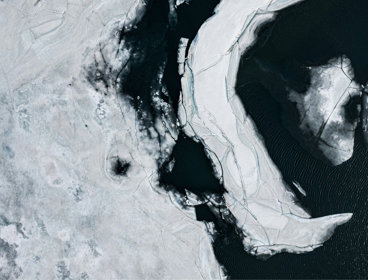 An aerial view of fragmented ice sheets floating on dark, cold waters.