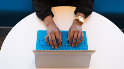 A person typing on a laptop positioned on a round, white table.