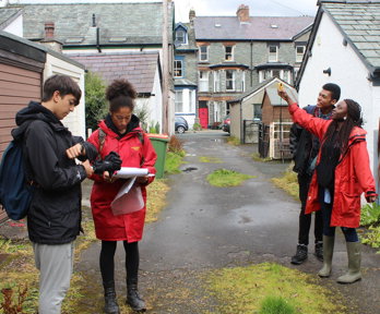 Group of young people taking measurements in a lane behind a row of houses.
