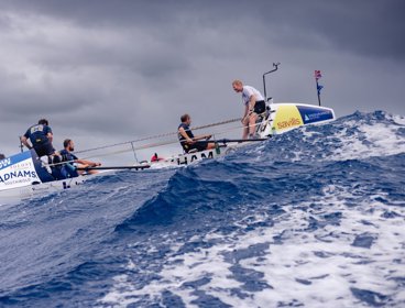 Row boat at sea amidst high waves and dark clouds.