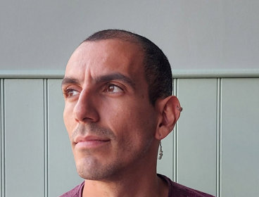 Person wearing a maroon shirt sitting against a light green paneled wall.