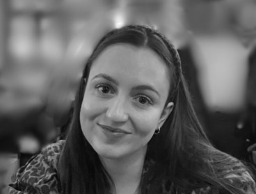 Person with hair wearing a leopard print top sitting indoors with blurred background lights.