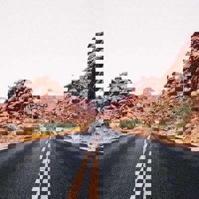 A Nevada road stretching out into the distance, the yellow central lines weaving slightly where the road bends. The road has rocky outcrops either side and in the distance