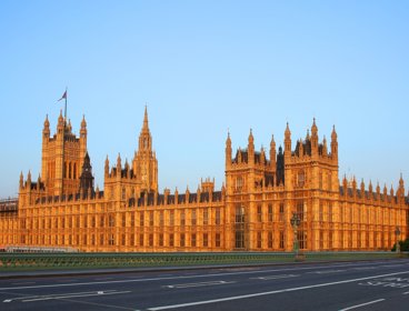Photograph of the houses of parliament taken from the adjacent bridge with a double-decker bus crossing the bridge.