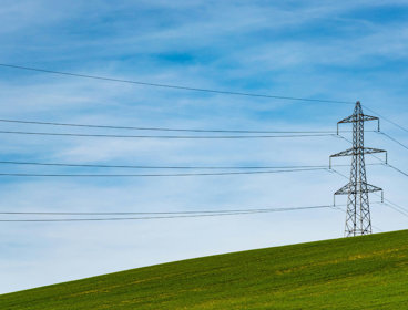 Sole electrical tower on grass field with blue sky.
