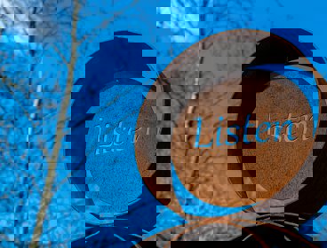 A sign saying ' listen' on a background of blue skye and leafless trees