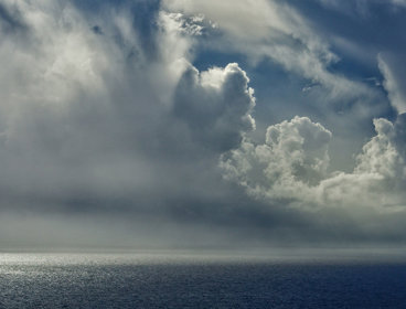 Moody grey clouds forming over the sea, light bouncing off the edges of the clouds.