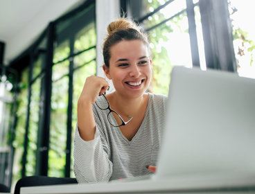 Person holding glasses smiling while looking at a laptop screen.