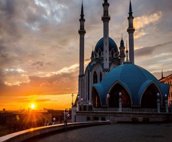 The sun is setting over ornate Russian buildings, which have arched windows, thin towers and turrets
