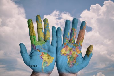 Hands that have a world map projected on to them, showing palm side round. The background is a cloudy blue sky