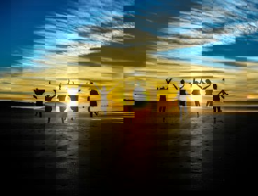 Group of five people jumping on a beach at sunset. The sun is in the front, making the people look like black silhouettes.